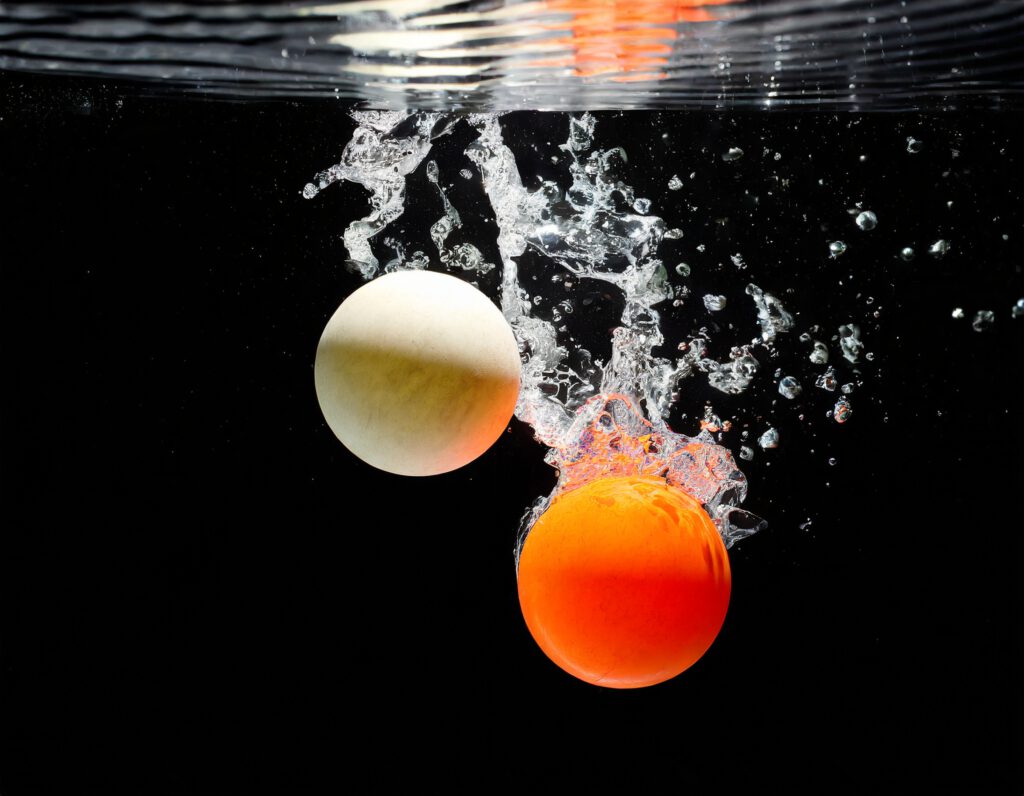 Generiert mit Adobe Firefly. two balls, ping pong; flying objects over water on black 64669.